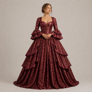 K&ouml;nnte beinhalten: Ein burgunderfarbenes Ballkleid mit quadratischem Ausschnitt und langen &Auml;rmeln mit R&uuml;schenb&uuml;ndchen. Das Kleid hat ein figurbetontes Oberteil und einen weiten Rock mit mehrschichtigen Details. Der Stoff hat ein dezentes Blumenmuster.
