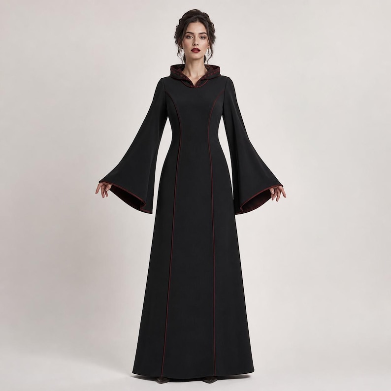 May include: A floor-length black dress featuring a hood, long flared bell sleeves, and a fitted bodice. The garment is accented with thin dark red piping along the hood, the sleeve edges, and vertical seams running down the front of the dress.