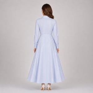 May include: A long-sleeved, floor-length dress featuring a light blue and white vertical striped pattern. The garment has a collared neckline, a fitted bodice with a defined waistline, and a full, flared skirt that extends to the floor.