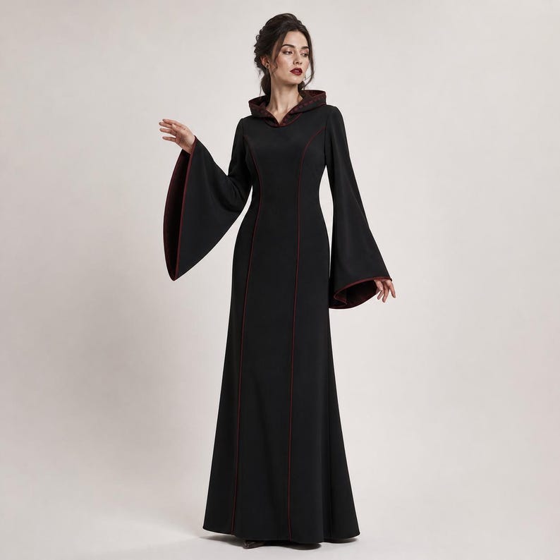 May include: A floor-length black dress featuring a hood, long flared bell sleeves, and a fitted bodice. The garment is accented with thin dark red piping along the seams, the hood edge, and the sleeve cuffs, creating a structured silhouette.