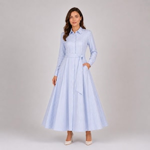 May include: A long-sleeved shirt dress featuring a light blue and white vertical striped pattern. The dress has a classic collar, a full button-down front, and a matching fabric tie belt at the waist, flowing into a wide, floor-length skirt.