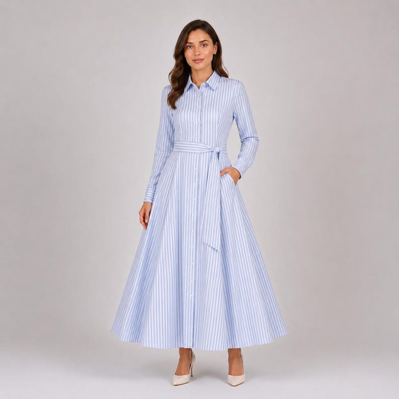 May include: A long-sleeved shirt dress featuring a light blue and white vertical striped pattern. The dress has a classic collar, a full button-down front, and a matching fabric tie belt at the waist, flowing into a wide, floor-length skirt.