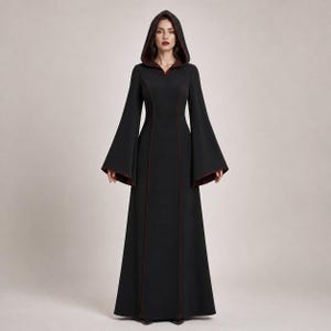 May include: A floor-length black hooded dress featuring long, wide bell sleeves and a deep red lining visible along the hood, sleeve cuffs, and vertical seams. The garment has a fitted bodice that flows into a straight, full-length skirt.