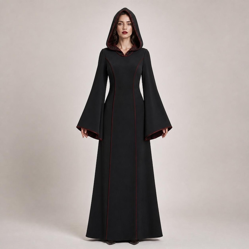 May include: A floor-length black hooded dress featuring long, wide bell sleeves and a deep red lining visible along the hood, sleeve cuffs, and vertical seams. The garment has a fitted bodice that flows into a straight, full-length skirt.