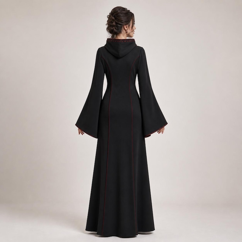 May include: A floor-length black dress featuring a hood, long flared bell sleeves, and thin dark red piping along the seams. The garment has a fitted bodice that transitions into a flared skirt, showcasing a solid black fabric throughout.