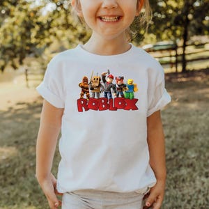 a young girl standing in front of a couch wearing a roblox shirt