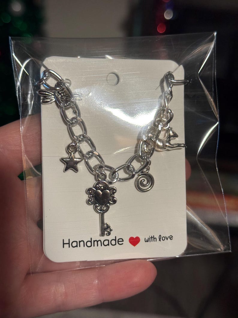 May include: Silver charm bracelet with a key, star, and spiral charms. The bracelet is presented on a white card with the text "Handmade with love" and a red heart. The bracelet is in a clear plastic bag.