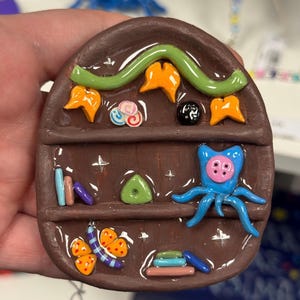 Unique clay mini bookshelf inspired by Coraline’s bedroom and themes. Made with oven bake clay and cured with resin for shine & protection.