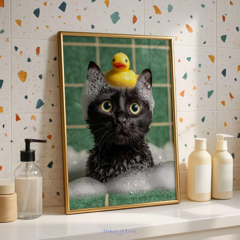 May include: A framed print features a black cat in a bubble bath, wearing a yellow rubber ducky on its head. The cat is surrounded by suds, with a green background and a gold frame. The print is displayed on a white surface.