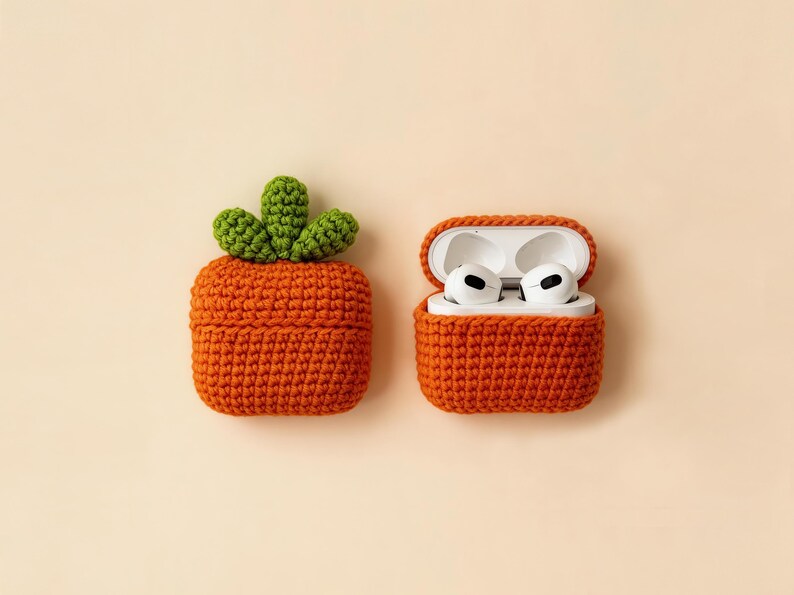 Two orange crochet cases, one closed and one open, designed to hold wireless earbuds. The closed case has a green crochet carrot top. The open case displays white earbuds. The cases are on a cream background.