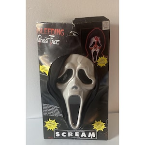 Puede incluir: Una máscara "Bleeding Ghost Face" de la película "Scream" en su embalaje original. La máscara es blanca con cuencas de ojos negras y una boca muy abierta. El embalaje es negro con el título de la película y detalles de la máscara.