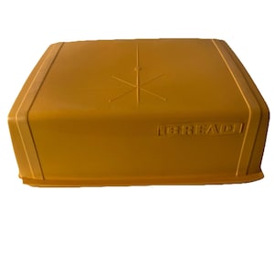 May include: Mustard yellow bread box with a starburst design on the lid. The box has a rectangular shape with rounded edges and the word "LIBREADI" embossed on the side.