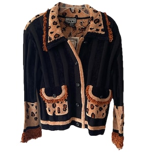 Könnte beinhalten: Schwarz-beiger gestreifter Cardigan mit Leopardenmuster. Der Cardigan hat eine Knopfleiste, zwei Vordertaschen mit Fransen und Leopardenmuster am Kragen und an den Ärmeln. Die Ärmel haben auch Fransen.