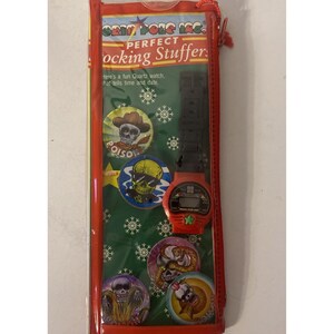 Può includere: Un orologio digitale rosso con cinturino nero e bottoni a tema teschio, confezionato in una custodia di plastica trasparente. Il testo "PERFECT Stocking Stuffer" è visibile.
