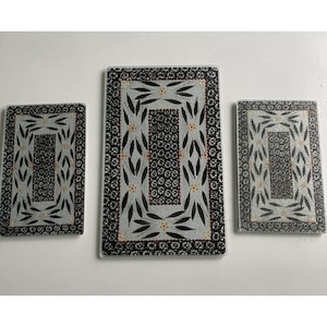 May include: Set of three rectangular glass cutting boards. Each board features a black and white floral design with a central rectangular pattern. The borders are black with a repeating pattern. The largest board is approximately 12 inches long.