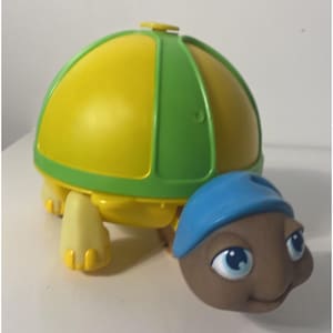 May include: A brightly coloured toy turtle. The shell is yellow with green edging, and the head is brown with a blue hat. The turtle has blue eyes and yellow feet. A cheerful toy for kids.