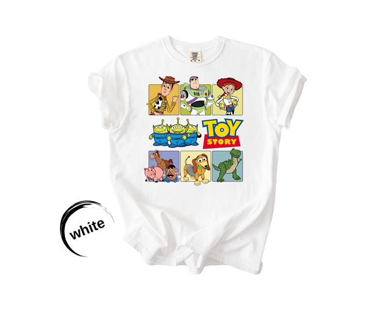May include: A white short-sleeved t-shirt featuring a colorful graphic print of Toy Story characters including Woody, Buzz Lightyear, Jessie, the green aliens, Bullseye, Hamm, Mr. Potato Head, Slinky Dog, and Rex, with the Toy Story logo.