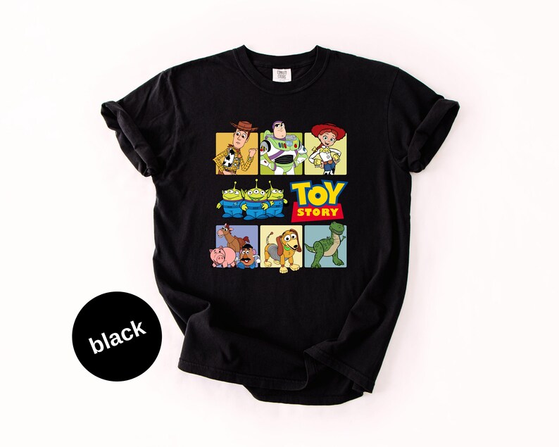 May include: A black short-sleeve t-shirt featuring a graphic print of Toy Story characters including Woody, Buzz Lightyear, Jessie, the Aliens, Bullseye, Hamm, Mr. Potato Head, Slinky Dog, and Rex, with the Toy Story logo in the center.