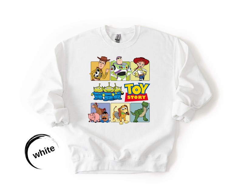 May include: A white crewneck sweatshirt featuring a colorful graphic print of Toy Story characters including Woody, Buzz Lightyear, Jessie, the Aliens, Hamm, Mr. Potato Head, Slinky Dog, and Rex, with the Toy Story logo printed in the center.