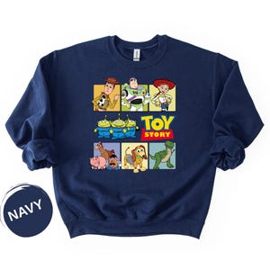 May include: A navy blue crewneck sweatshirt featuring a graphic print of Toy Story characters including Woody, Buzz Lightyear, Jessie, the Aliens, Bullseye, Hamm, Mr. Potato Head, Slinky Dog, and Rex, with the yellow and red Toy Story logo text.