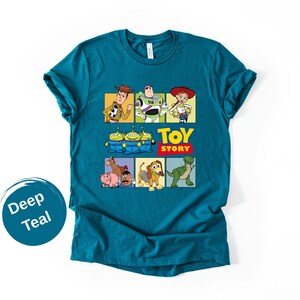 May include: A deep teal short-sleeve t-shirt featuring a graphic print of Toy Story characters including Woody, Buzz Lightyear, Jessie, the Aliens, Hamm, Mr. Potato Head, Slinky Dog, and Rex, with the Toy Story logo printed in yellow and red.