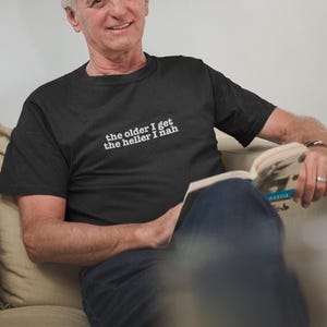 May include: A black short-sleeved t-shirt featuring white text printed on the chest that reads, the older I get the heller I nah. The shirt has a crew neckline and a standard fit, constructed from a solid-colored fabric with a simple design.