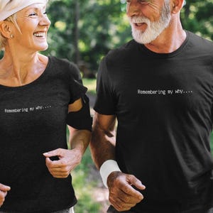 May include: Two black short-sleeved t-shirts featuring the white text "Remembering my why...." printed on the chest. The shirts have a crew neckline and a standard fit, designed for athletic activity with a simple, clean aesthetic and minimal design.