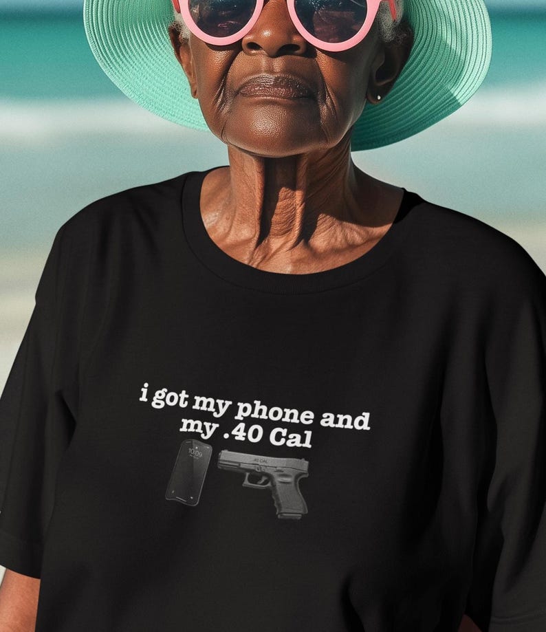 May include: A black short-sleeved t-shirt featuring white text that reads, "i got my phone and my .40 Cal," accompanied by a graphic illustration of a black smartphone and a black handgun positioned directly below the printed text.