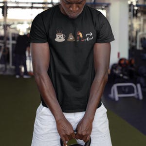 May include: Black t-shirt with a humorous graphic. The graphic includes a coffee cup with a mustache, a pile of poop, a person exercising, and a repeating arrow symbol. The person in the image is wearing white shorts and holding a kettlebell.