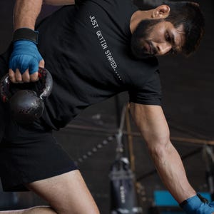May include: A white ceramic mug with a black handle and the text "But First, Coffee" in a bold, black font. The mug is set against a blurred background, suggesting a cozy setting.