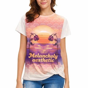 Puede incluir: Camiseta blanca de manga corta con un gráfico de puesta de sol y el texto "Melancholy aesthetic". El diseño incluye una puesta de sol sobre el agua con flores. La camiseta está anudada en la cintura.