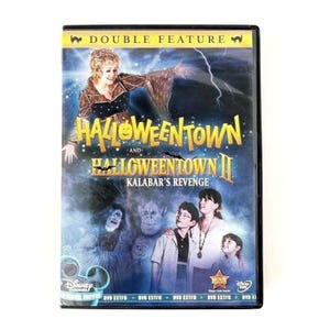 May include: A double feature DVD case for Halloweentown and Halloweentown II: Kalabar's Revenge. The cover art features a woman in a dark dress, a group of children, and various fantasy creatures against a dark, stormy blue background with lightning.