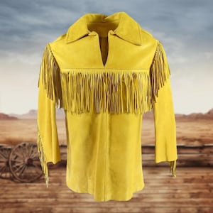 May include: Mustard yellow suede jacket with long sleeves and a notched collar. The jacket features long fringe across the chest and on the sleeves. The background shows a western landscape with a wooden fence and wagon wheels.