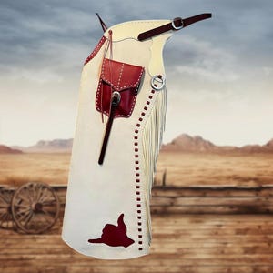 May include: Cream-colored leather chaps with red accents, a small pouch, and fringe detailing. The chaps feature a red hand-shaped design and are secured with buckles. The background shows a western landscape.