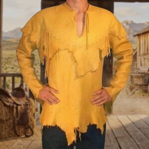 May include: A long-sleeved yellow suede shirt featuring a V-neckline with a lace-up detail, a decorative yoke with fringe trim across the chest and shoulders, and an uneven, raw-cut hemline that falls below the waistline.