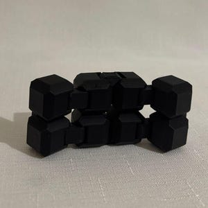 May include: A black fidget toy made of connected geometric cubes. The cubes are a matte black and arranged in a flexible, articulated design. The toy is designed for manipulation and play, providing a tactile experience.