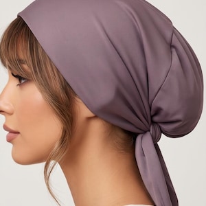 May include: A solid mauve head wrap featuring a smooth, matte fabric construction. The head covering is designed with a gathered back section and two long fabric ties that are knotted securely at the nape of the neck, creating a draped effect.