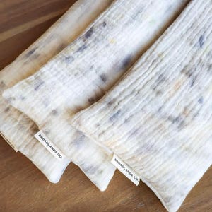 May include: Three off-white, textured fabric items with a speckled pattern in shades of gray, blue, and yellow. Each item has a tag that reads "BROADLANDS CO." The items are arranged on a wooden surface.