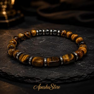 May include: A beaded bracelet featuring alternating round and rectangular tiger eye stones in shades of brown and gold, accented with small, polished metallic silver-tone spacers and dark, smooth spherical beads arranged in a circular pattern.