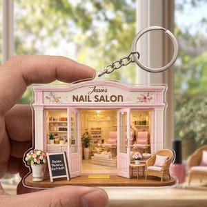 May include: A miniature nail salon keychain with a silver keyring. The salon is pink and white with the text "Jessie's NAIL SALON" above the entrance. A small chalkboard reads "Relax. Renew. Refresh."