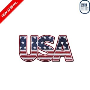 May include: An embroidered patch featuring the letters USA in a bold font. The design incorporates the American flag pattern with a dark blue field containing white stars on the upper sections and horizontal red and white stripes below.
