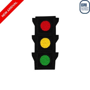 May include: Embroidered patch featuring a black traffic light with red, yellow, and green circles. The patch has a rectangular shape with rounded corners. The words "NEW ARRIVAL" are printed on a red diagonal banner.