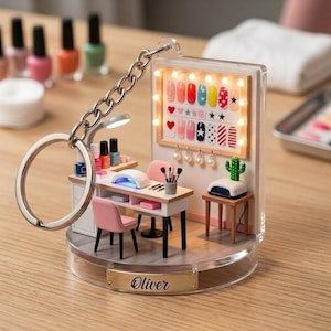 May include: Miniature nail salon keychain with a detailed interior. Features a display of painted nails, a small table with tools, and a pink chair. The keychain has a silver chain and a gold nameplate that reads "Oliver".