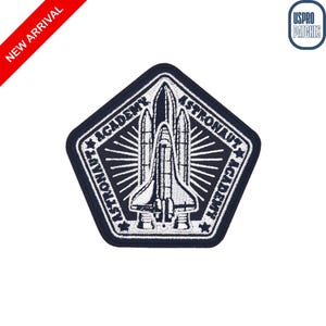 May include: A navy blue and white embroidered patch in a pentagon shape. The patch features a detailed illustration of a space shuttle with the words "Astronaut Academy" around the edges. The words "New Arrival" are on a red diagonal banner.