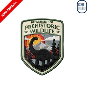 May include: Embroidered patch featuring a black dinosaur silhouette against a sunset and mountain backdrop. The patch reads "DEPARTMENT OF PREHISTORIC WILDLIFE" in green text. A red diagonal banner reads "NEW ARRIVAL".