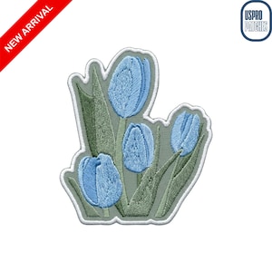 May include: Embroidered patch featuring four light blue tulip buds with green leaves. The patch has a light green background and a white border. The words "NEW ARRIVAL" are printed diagonally in red. The patch is from USPRO PATCHES.