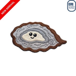 May include: An embroidered patch shaped like an oyster with a brown outer edge, a textured gray shell, and a cream-colored center featuring a small, smiling face with two black eyes and a curved mouth. The patch includes a small logo in the corner.