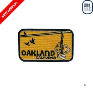 May include: Embroidered patch with a yellow background featuring the word "OAKLAND CALIFORNIA" and a pair of hanging sneakers. Two birds are flying above the text. The patch has a black border and is labeled "NEW ARRIVAL".