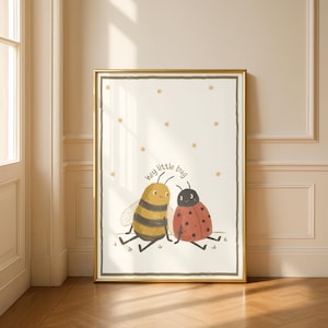 May include: A framed print with a cartoon bee and ladybug. The bee is yellow and black striped, the ladybug is red with black spots. The text "hey little bug" is above them, with gold stars scattered around the image.