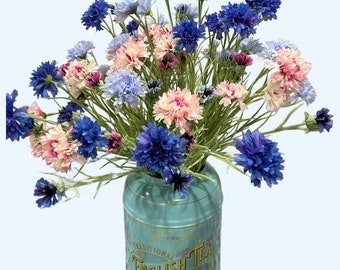 May include: A bouquet of blue and pink cornflowers in a vintage blue tin can with the text "Traditional English Tea Fine Breakfast Tea" printed on the side.